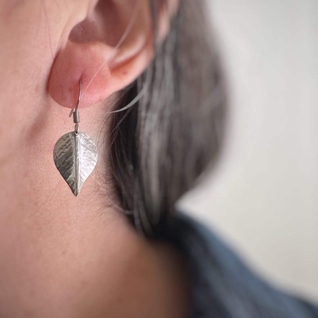 Medium, silver tone surgical steel leaf shaped earring on a french hook ear wire, shown as worn.