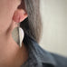 Extra large, silver tone surgical steel leaf shaped earring on a french hook ear wire, shown as worn.