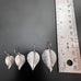 silvery surgical steel leaf earrings shown next to ruler to illustrate the four size options, .75", .90", 1", and 1.25".