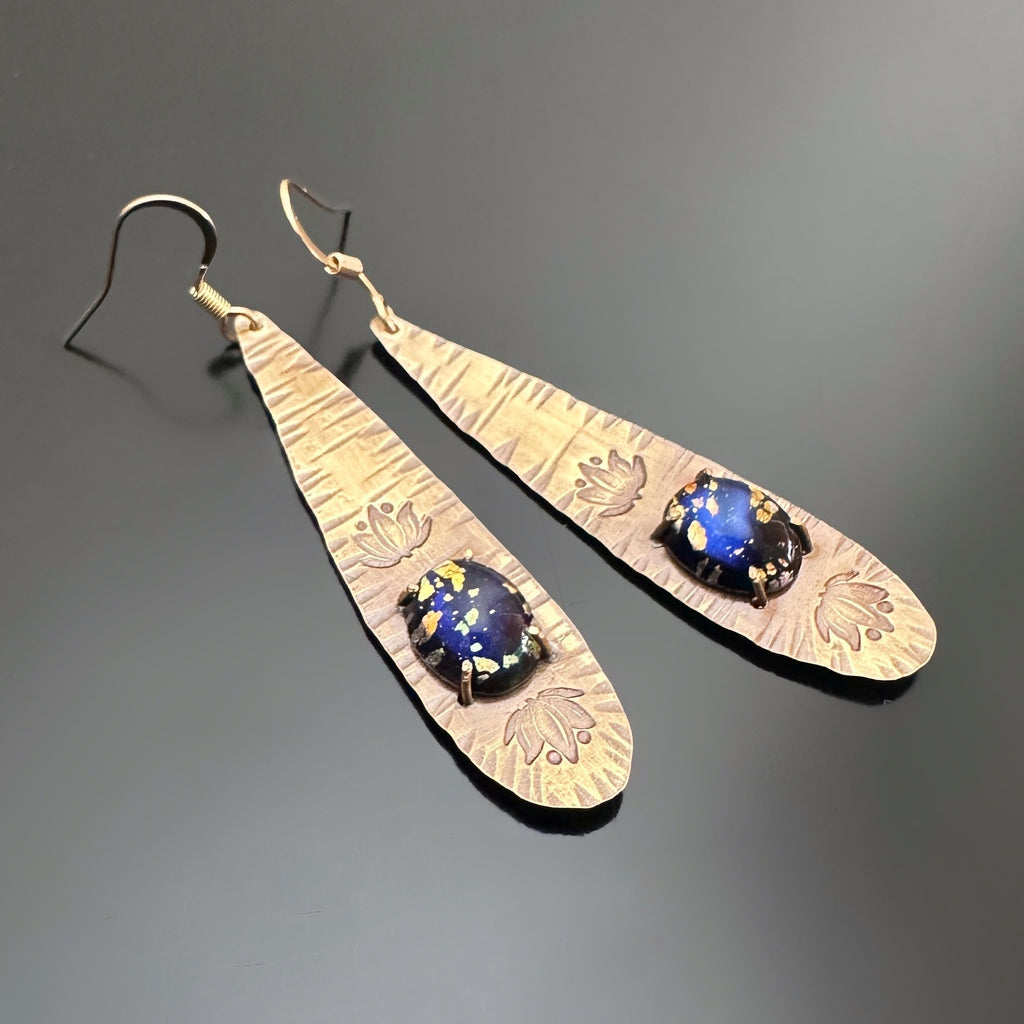 long brass teardrop earrings with french hook ear wires.  The tear drop has hammer marks and stamped lotus flowers with a focal of a midnight blue opal glass oval, prong-set near the bottom.