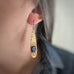 long brass teardrop earrings with french hook ear wires.  The tear drop has hammer marks and stamped lotus flowers with a focal of a midnight blue opal glass oval, prong-set near the bottom. shown as worn.