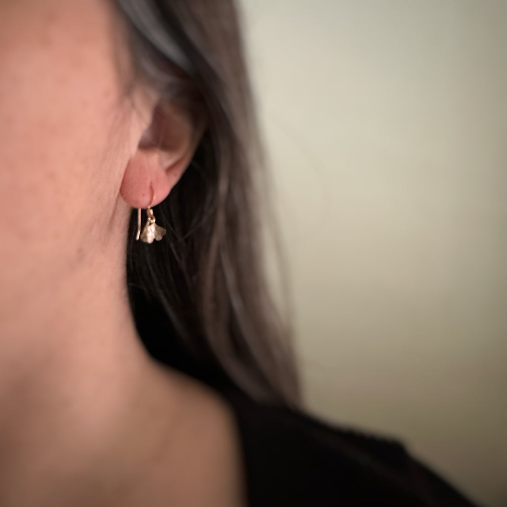 Tiny oxidized brass ginkgo leaf earrings shown on model.
