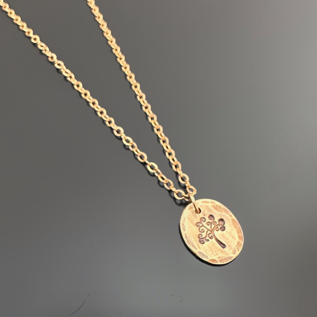 Golden antiqued brass necklace with an oval pendant with a hammered texture depicting a swirly tree.