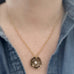Golden antiqued brass pendant in a wild rode motif with a small white freshwater pearl in the center.  The chain is a gold tone rolo style. Shown on model