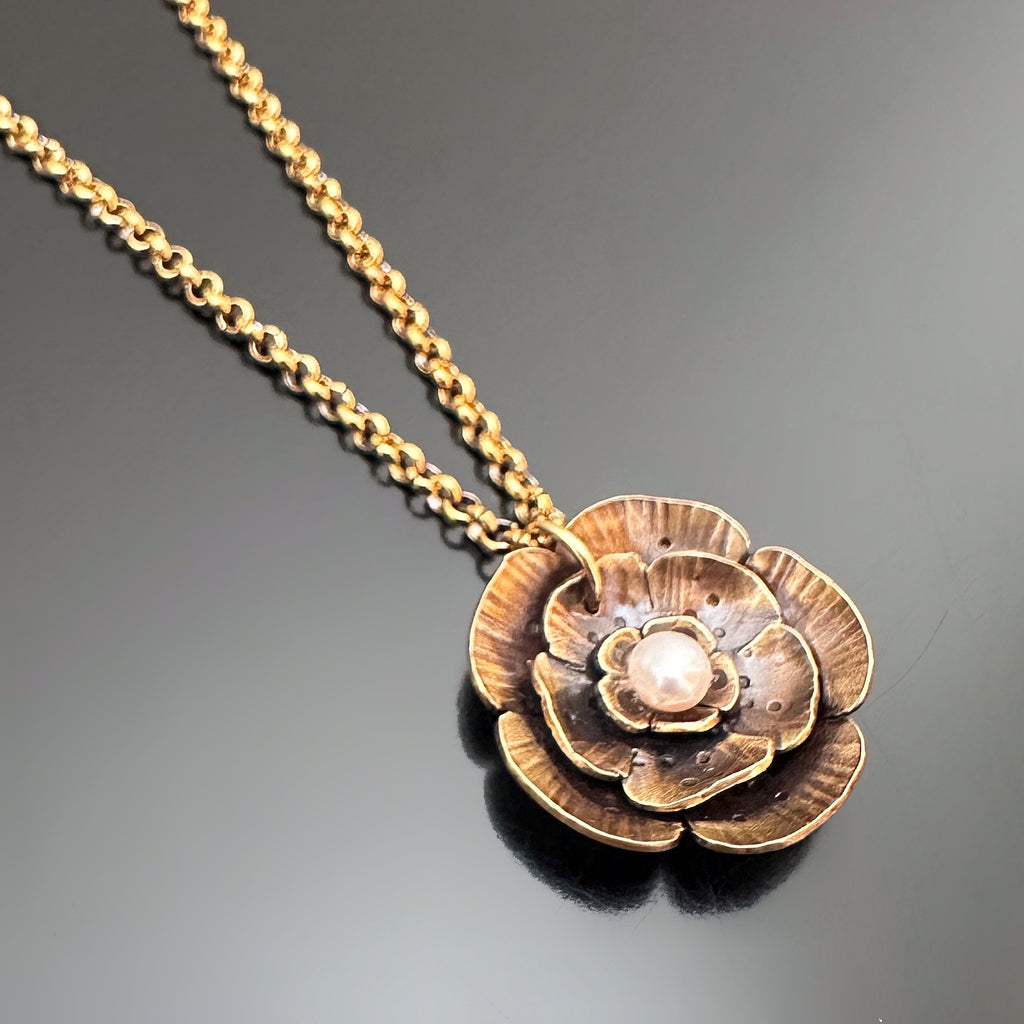 Golden antiqued brass pendant in a wild rode motif with a small white freshwater pearl in the center.  The chain is a gold tone rolo style.