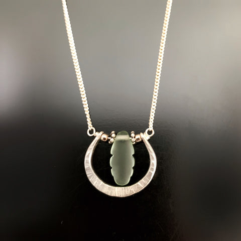 Hand formed sterling silver horseshoe shaped pendant with a frosted green glass feather drop.